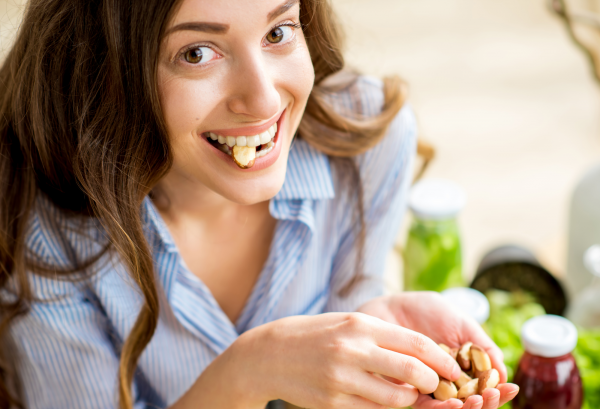 Mujer comiendo frutos secos mientras sonríe a cámara